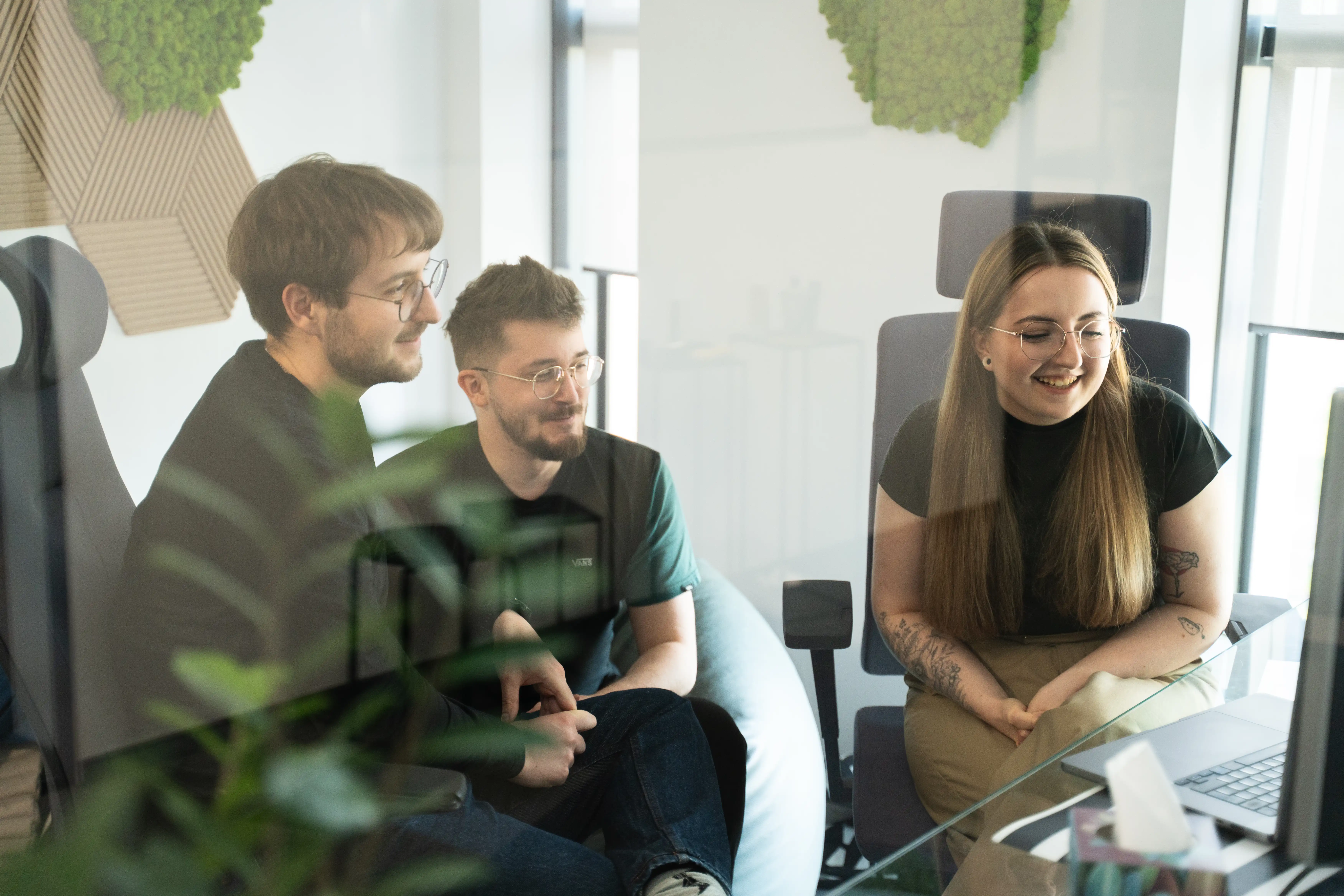 "Three data professionals sitting together in a modern office, smiling and looking at a laptop screen during a collaborative meeting."