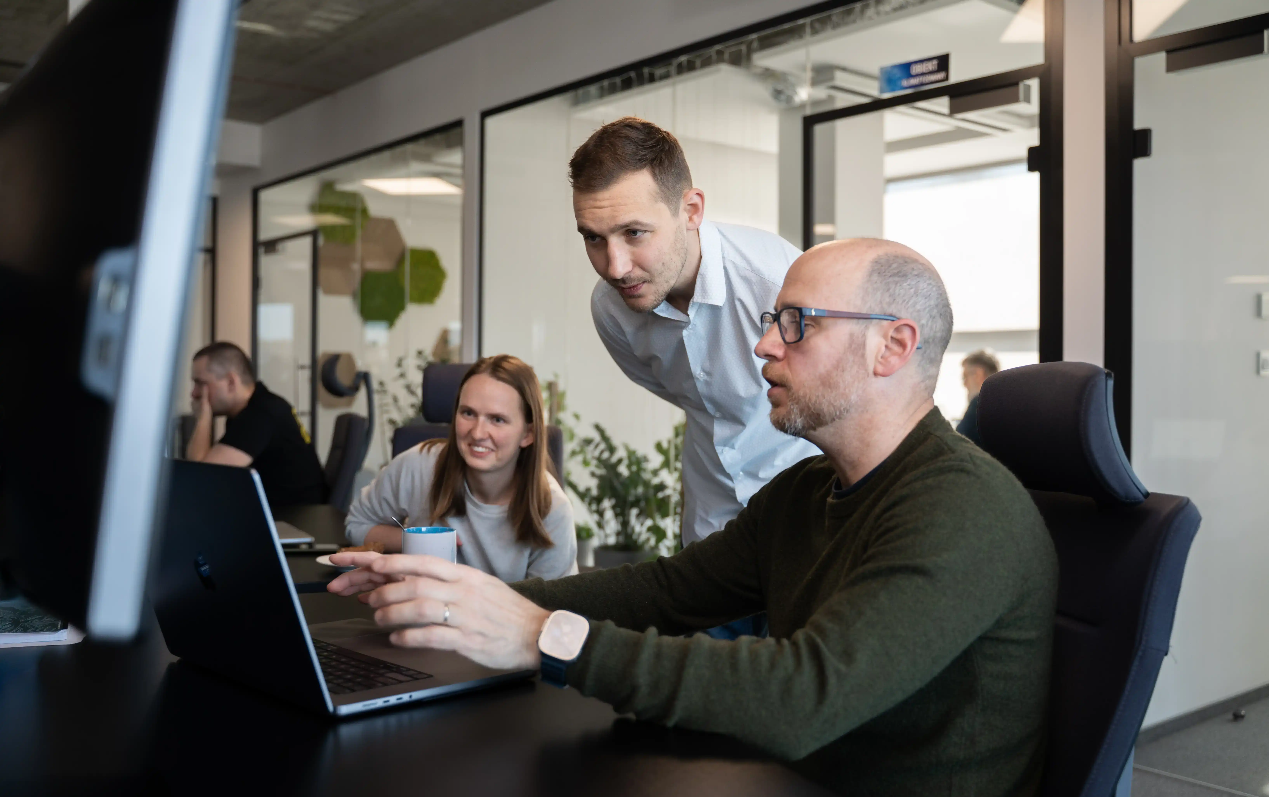 Three data professionals collaborating around a laptop in a modern office, discussing data strategy solutions.