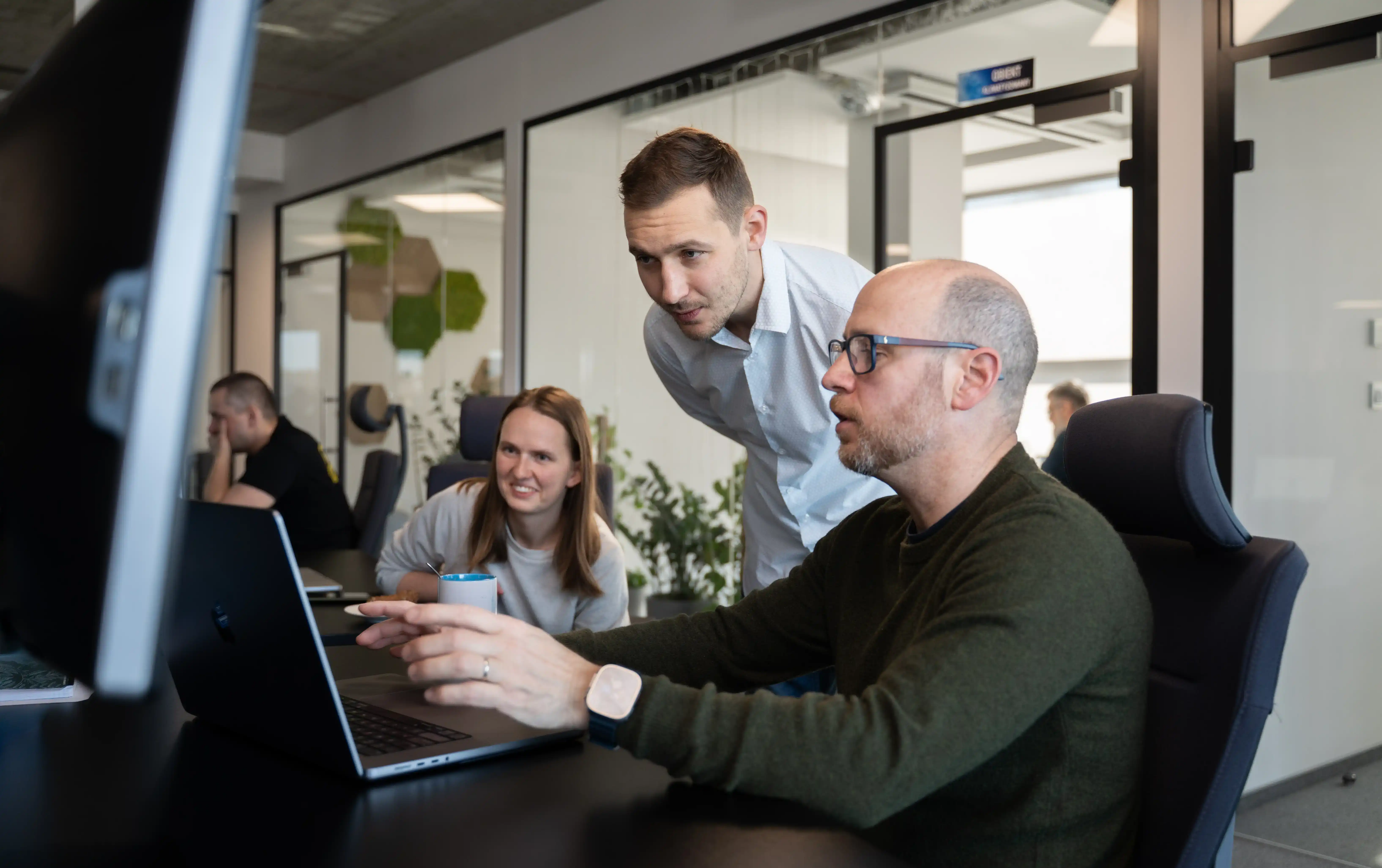 Three data professionals collaborating around a laptop in a modern office, discussing data strategy solutions.