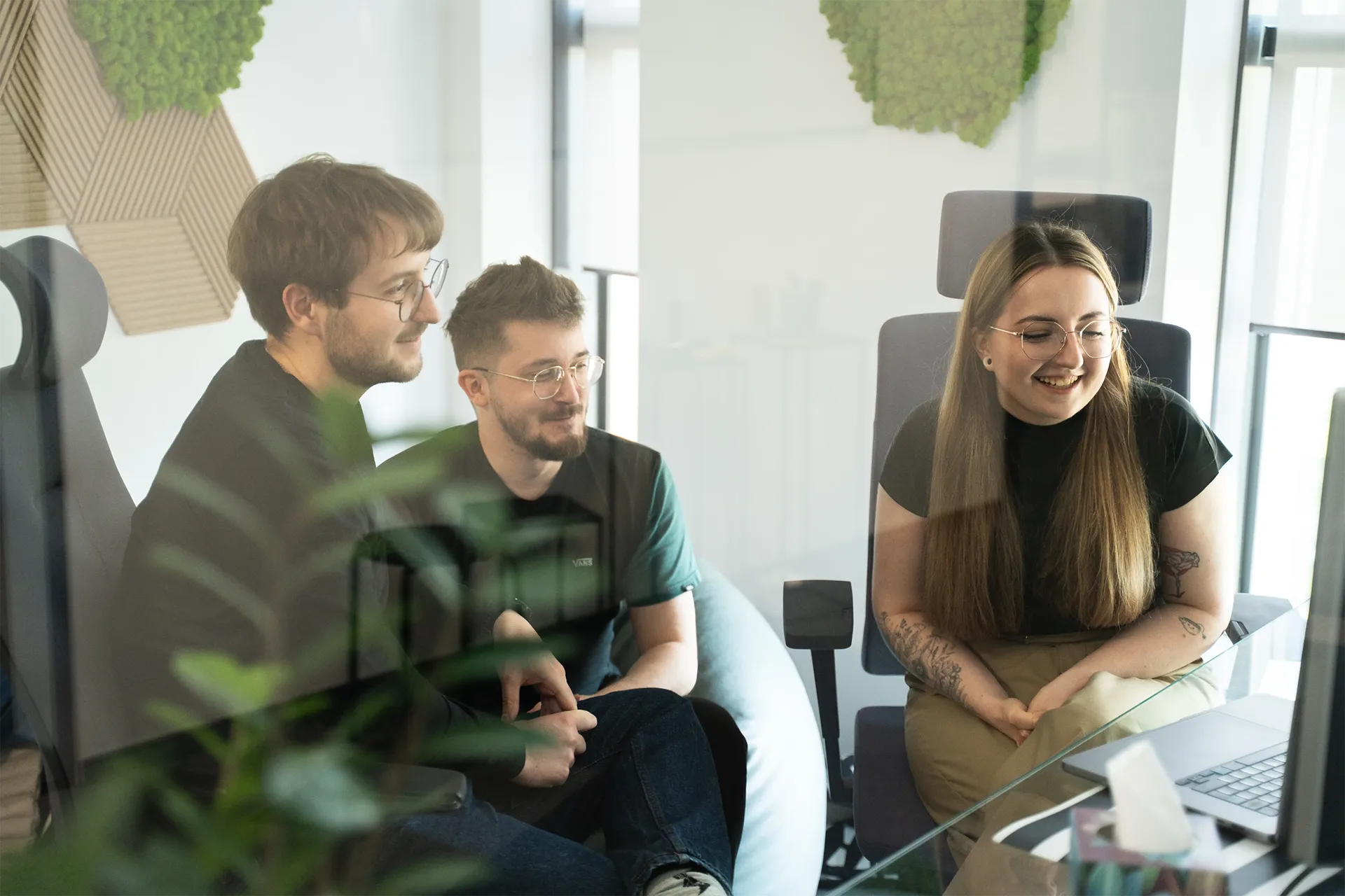 "Three data professionals sitting together in a modern office, smiling and looking at a laptop screen during a collaborative meeting."