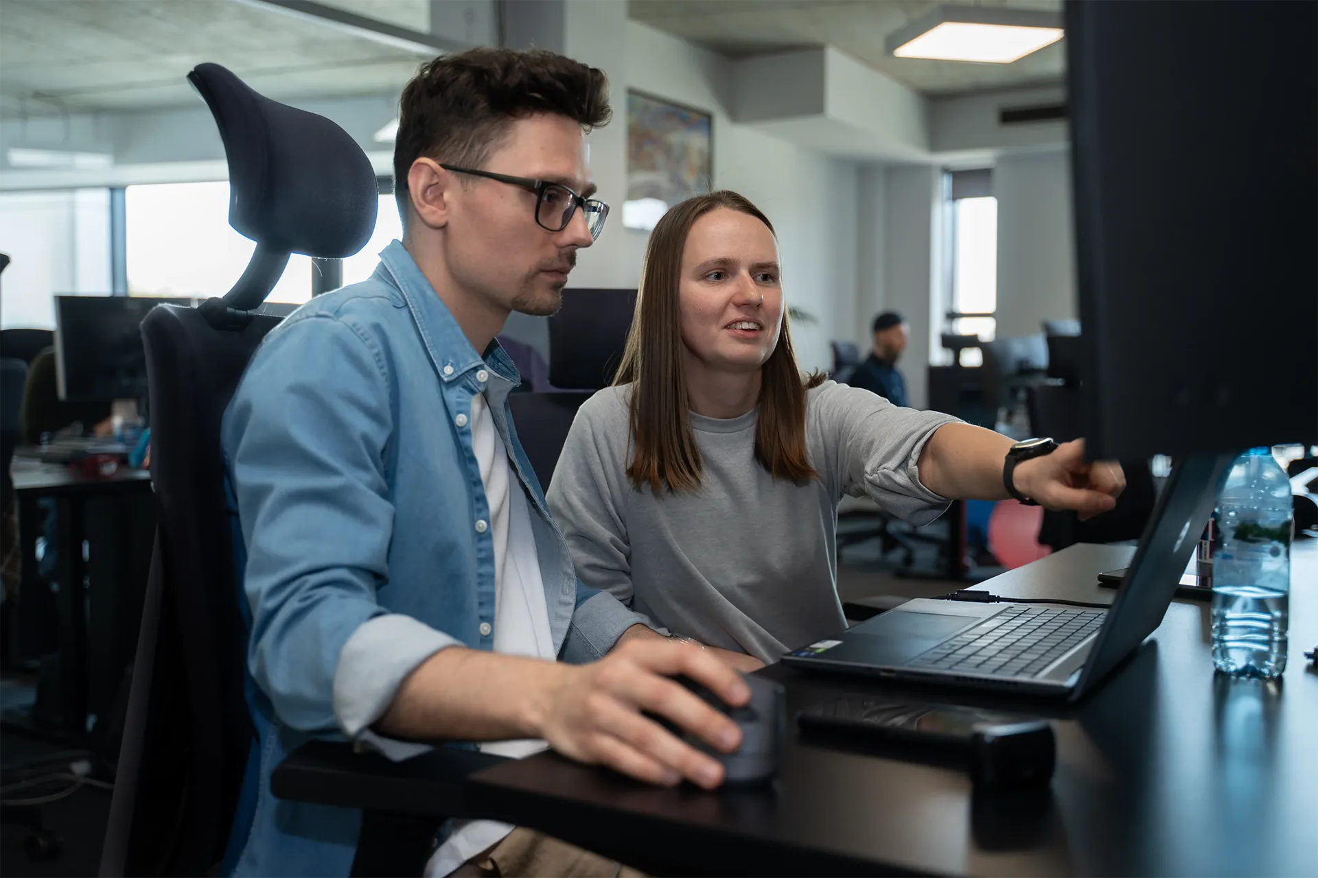 Two business professionals collaborating on data analytics projects using laptops in a modern office environment