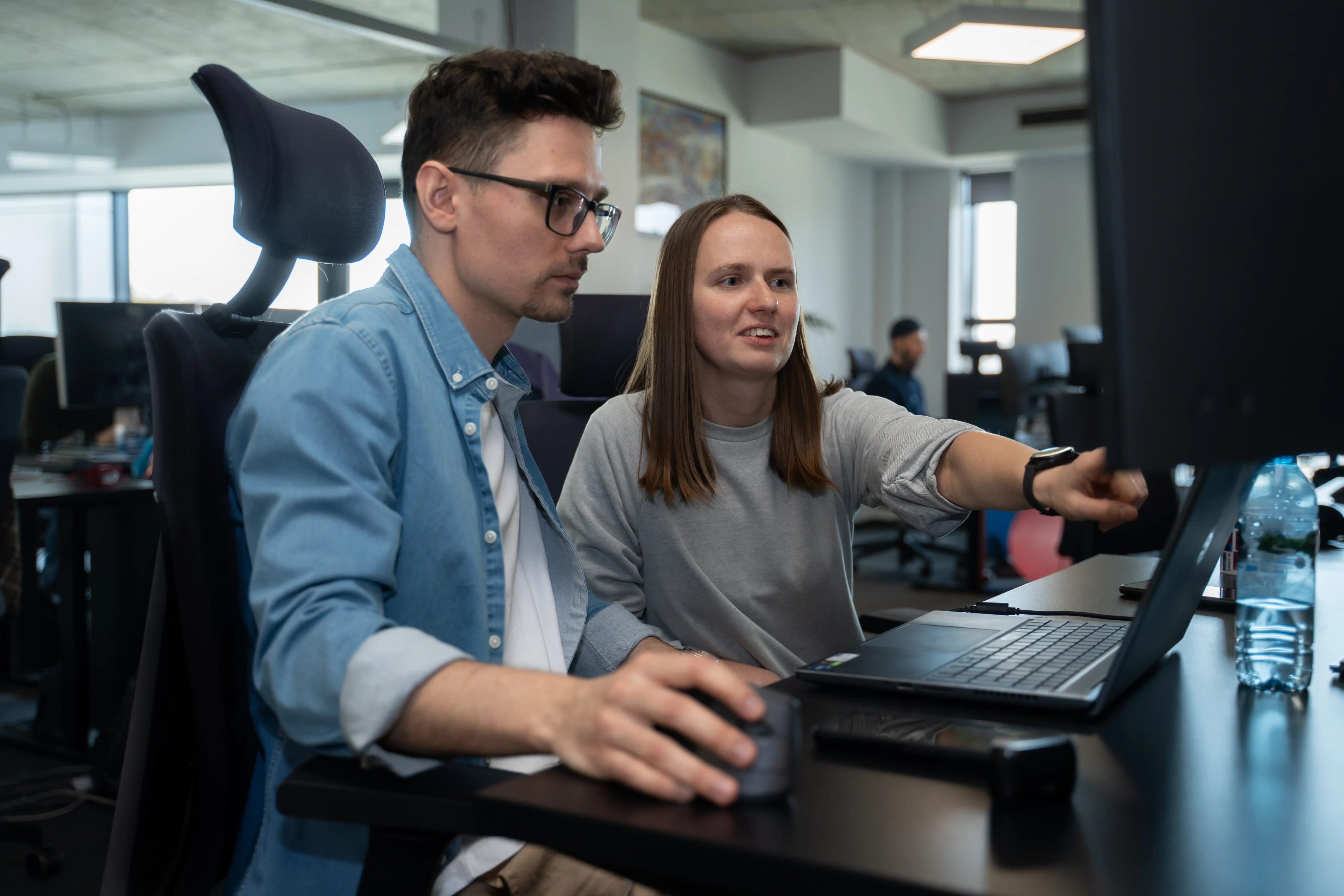 Two business professionals collaborating on data analytics projects using laptops in a modern office environment