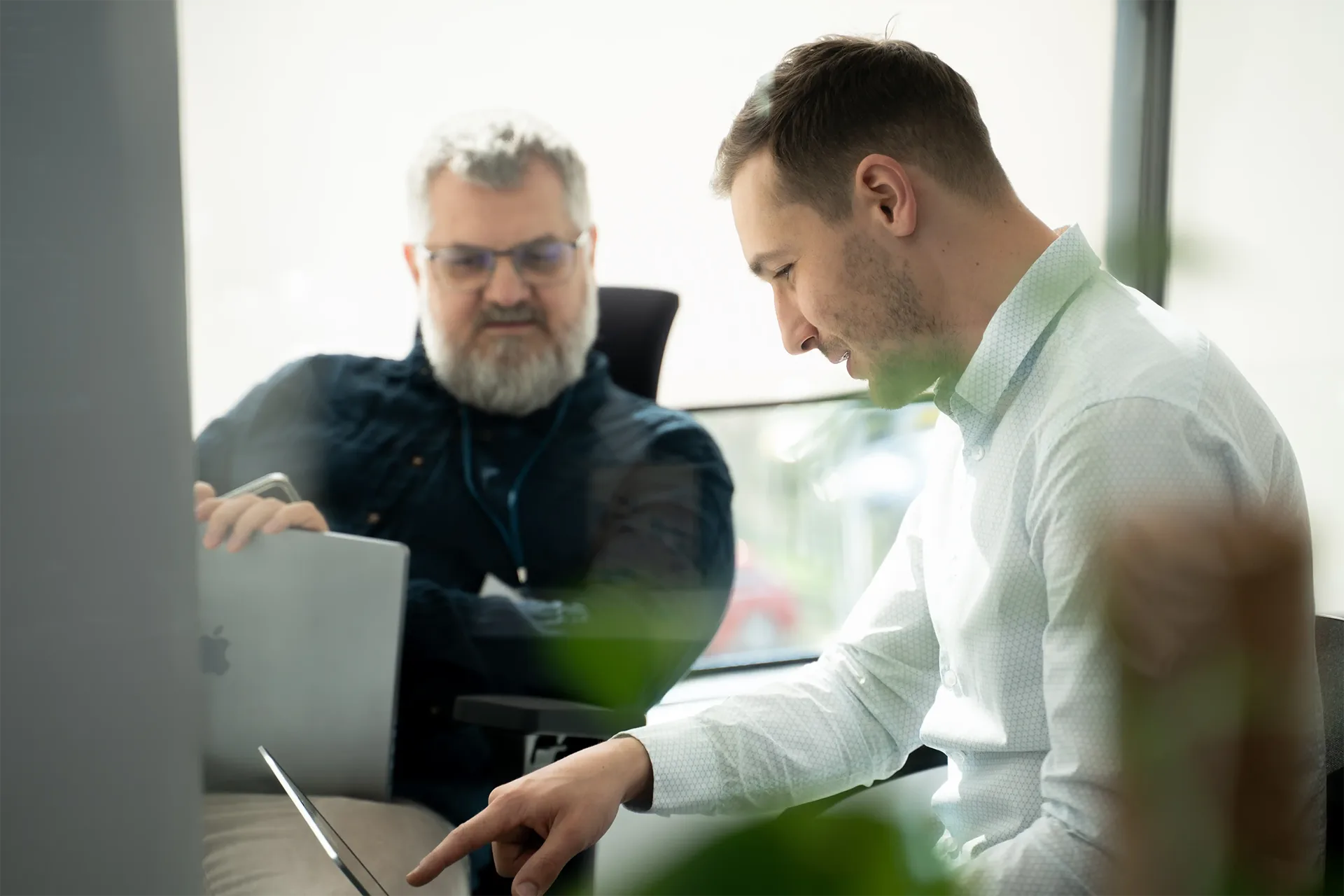 Two business professionals collaborating on data analytics projects using laptops in a modern office environment